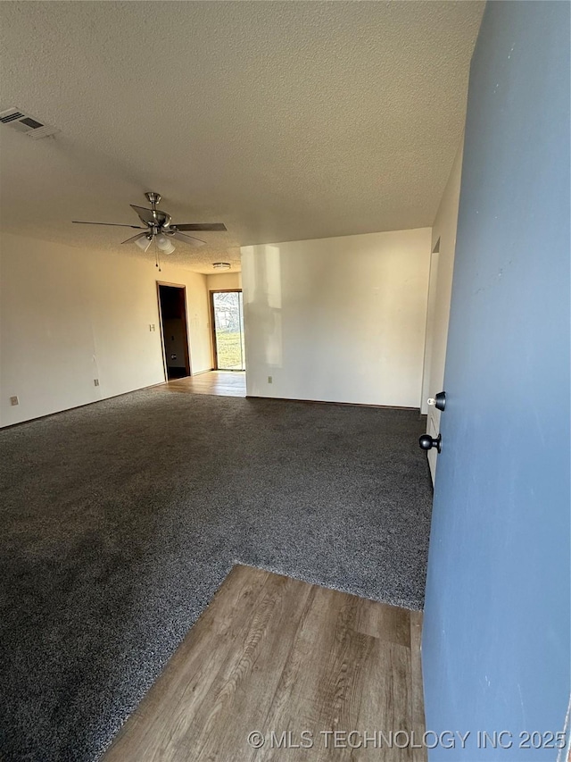 empty room featuring a textured ceiling, carpet, ceiling fan, and wood finished floors