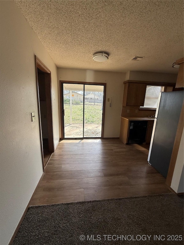 corridor featuring visible vents, a textured ceiling, dark wood finished floors, and a textured wall