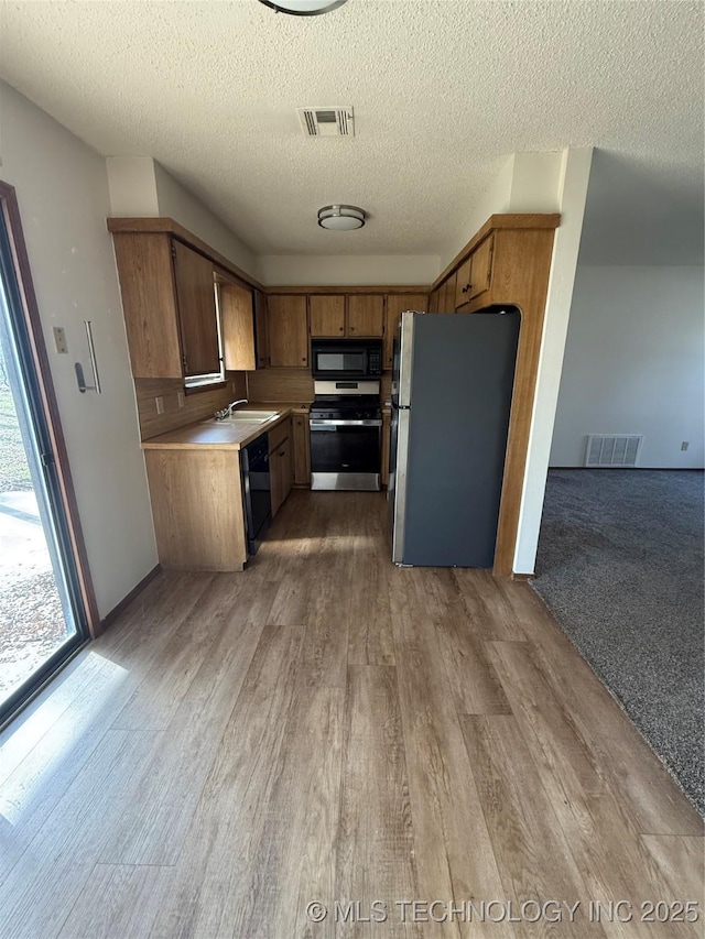 kitchen with a sink, visible vents, black appliances, and light wood finished floors