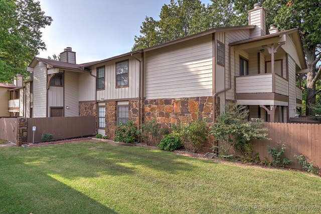 back of property featuring stone siding, a chimney, a yard, and fence