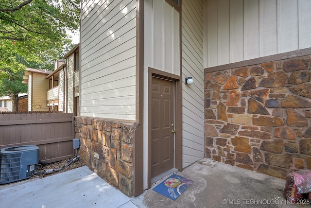 entrance to property featuring fence, central AC unit, and stone siding