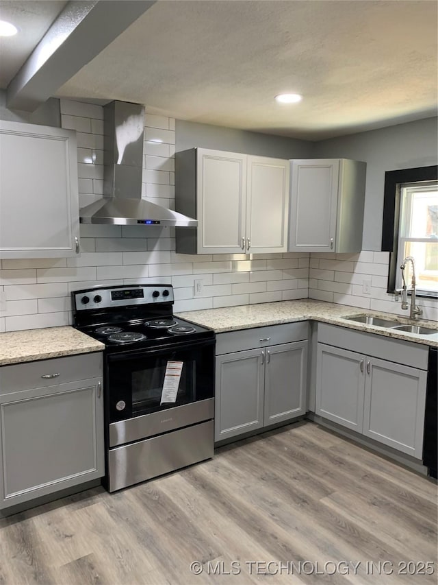 kitchen with wall chimney exhaust hood, electric stove, light wood-style floors, and a sink