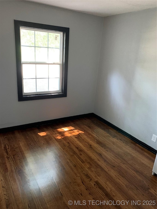 spare room with baseboards and dark wood-type flooring