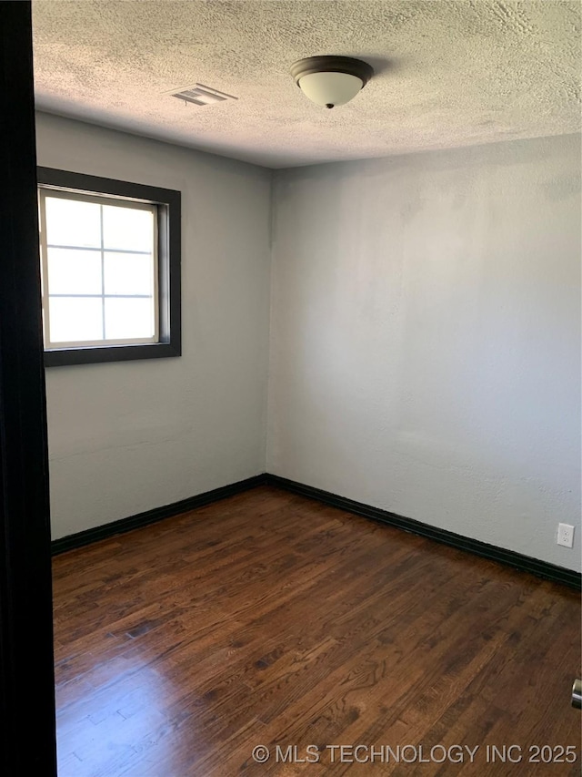 empty room featuring visible vents, baseboards, a textured ceiling, and dark wood finished floors