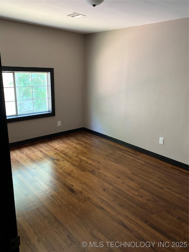 unfurnished room with visible vents, baseboards, and dark wood-style floors