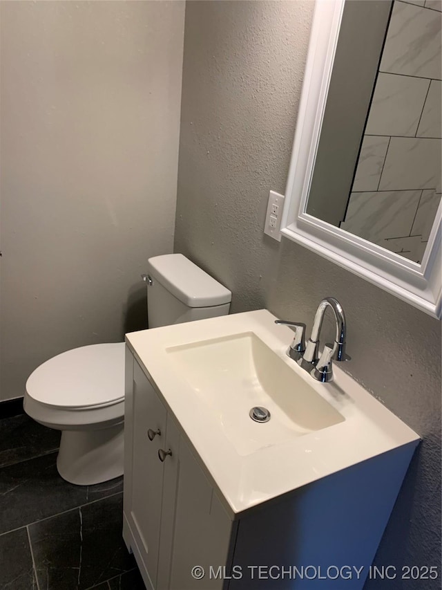 bathroom featuring toilet, vanity, and a textured wall