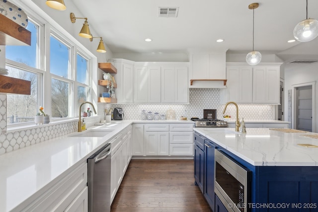 kitchen with visible vents, blue cabinetry, stainless steel appliances, a sink, and white cabinetry