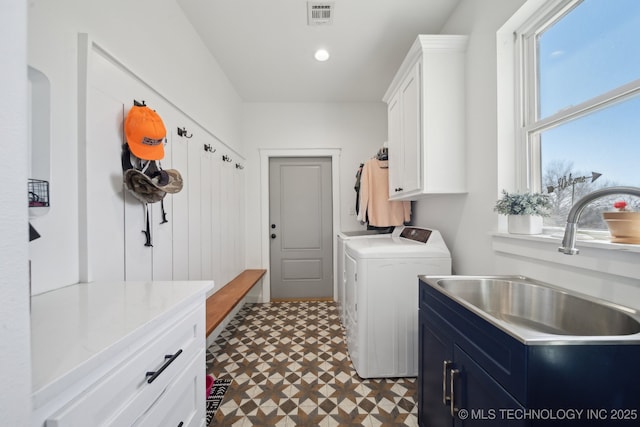 clothes washing area featuring visible vents, washer and clothes dryer, a sink, cabinet space, and dark floors