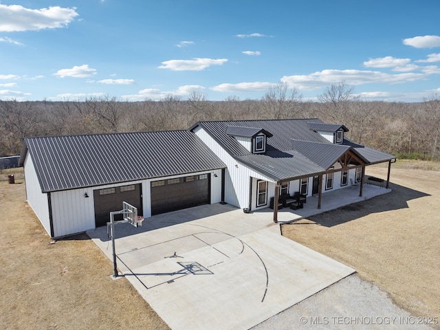 exterior space featuring driveway, metal roof, an attached garage, and a view of trees