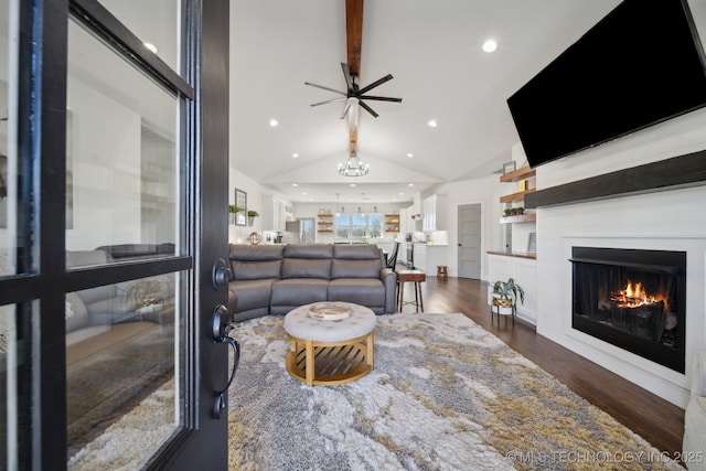 living area with lofted ceiling, recessed lighting, dark wood-style flooring, a lit fireplace, and ceiling fan with notable chandelier