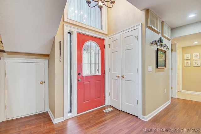 foyer entrance with visible vents, baseboards, a notable chandelier, and wood finished floors