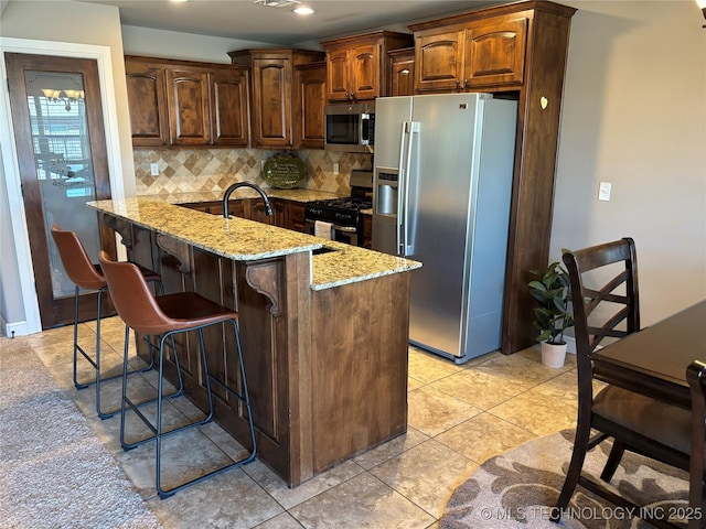 kitchen with tasteful backsplash, light stone countertops, a breakfast bar area, light tile patterned flooring, and stainless steel appliances