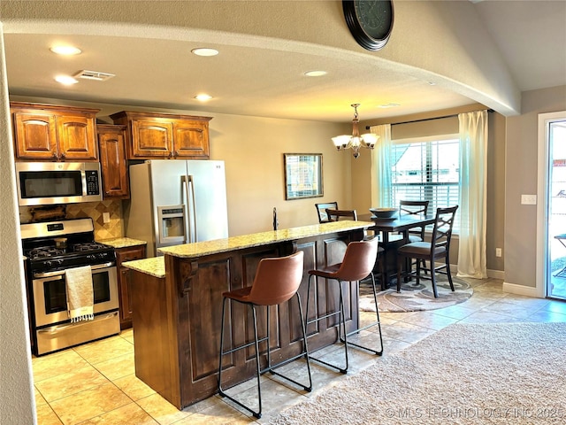 kitchen featuring visible vents, backsplash, light stone countertops, a kitchen bar, and appliances with stainless steel finishes