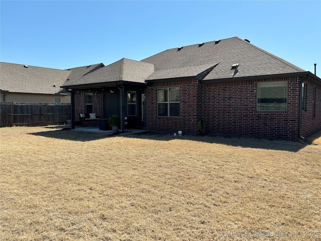 back of property featuring brick siding, a shingled roof, fence, a lawn, and a patio area