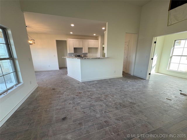 unfurnished living room with baseboards, dark wood finished floors, an inviting chandelier, a high ceiling, and recessed lighting