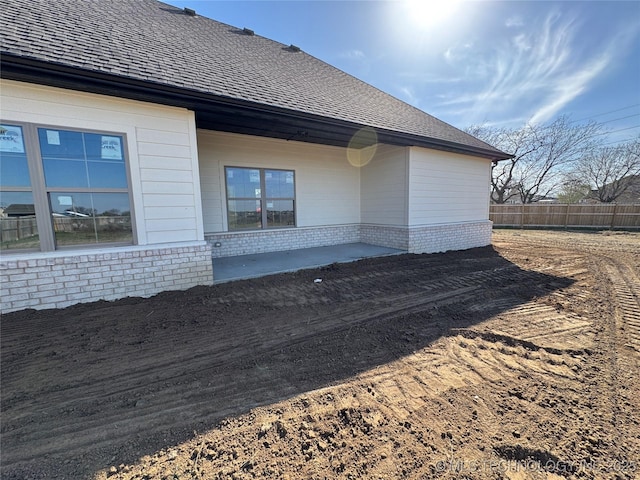 view of side of property with a patio area, fence, and a shingled roof