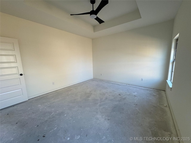 spare room featuring a tray ceiling, ceiling fan, and unfinished concrete floors