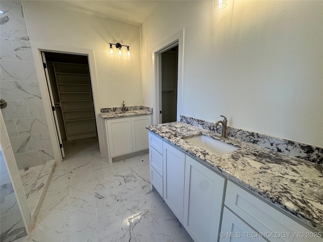 bathroom with two vanities, marble finish floor, a tile shower, and a sink