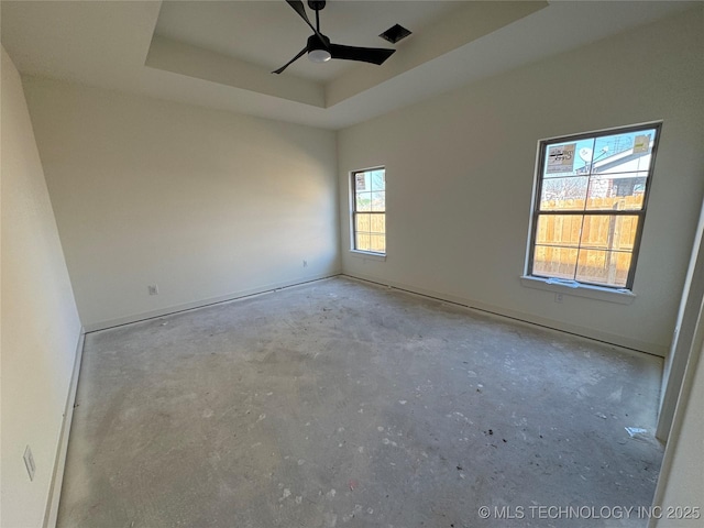 unfurnished room with ceiling fan, unfinished concrete floors, and a tray ceiling