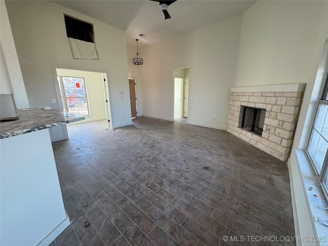 unfurnished living room featuring dark wood-type flooring, a ceiling fan, a high ceiling, a fireplace, and baseboards