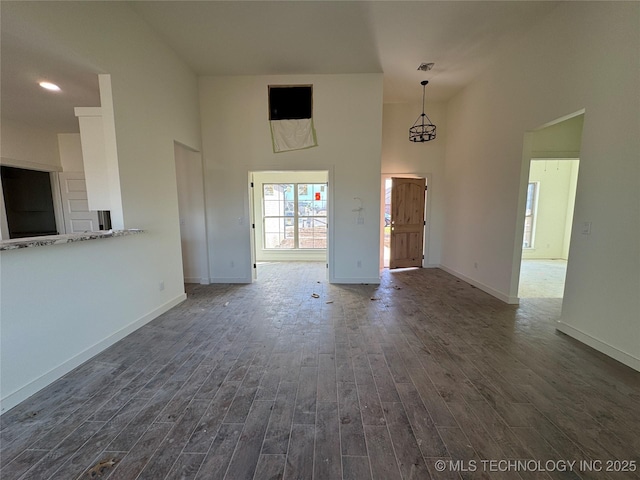 unfurnished living room featuring visible vents, baseboards, dark wood-type flooring, and a towering ceiling