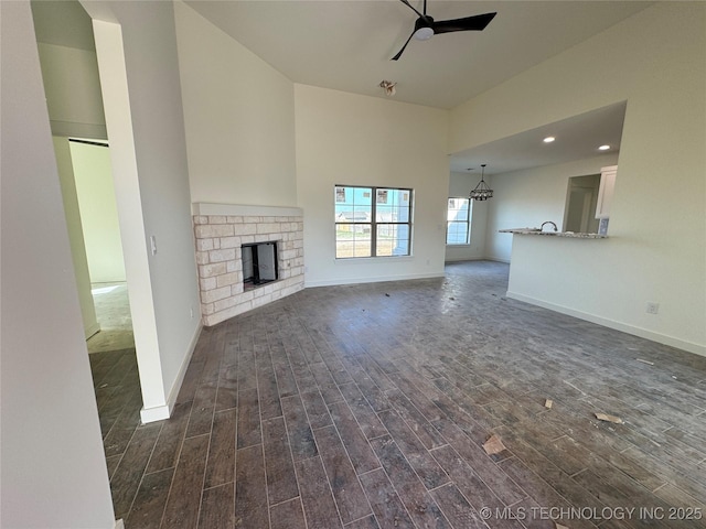 unfurnished living room with dark wood finished floors, ceiling fan with notable chandelier, a fireplace, and baseboards