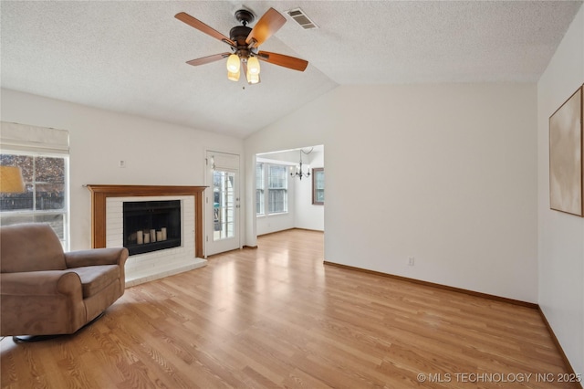 unfurnished living room with light wood-type flooring, visible vents, a textured ceiling, a fireplace, and vaulted ceiling