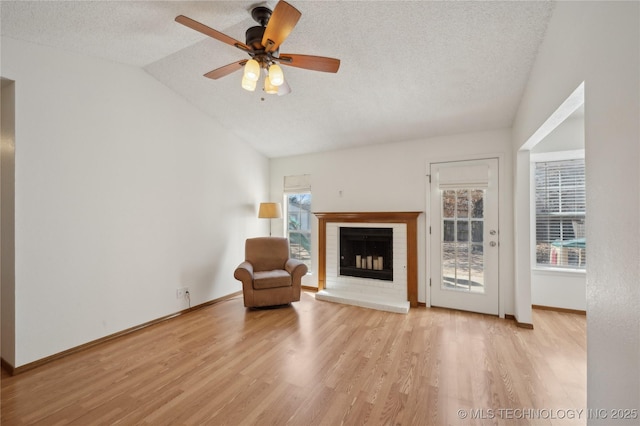 unfurnished room with a textured ceiling, a fireplace, light wood finished floors, baseboards, and vaulted ceiling