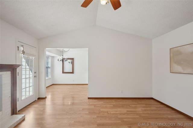 spare room with lofted ceiling, a fireplace, light wood-style floors, a textured ceiling, and ceiling fan with notable chandelier