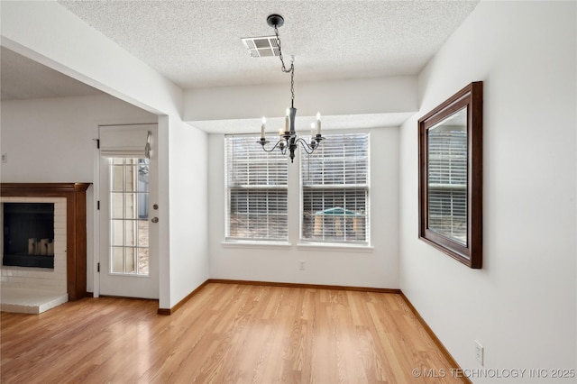 unfurnished dining area featuring visible vents, light wood-type flooring, a fireplace, an inviting chandelier, and a textured ceiling