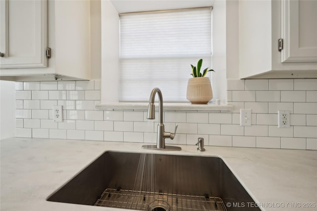 kitchen with white cabinetry, light stone counters, tasteful backsplash, and a sink