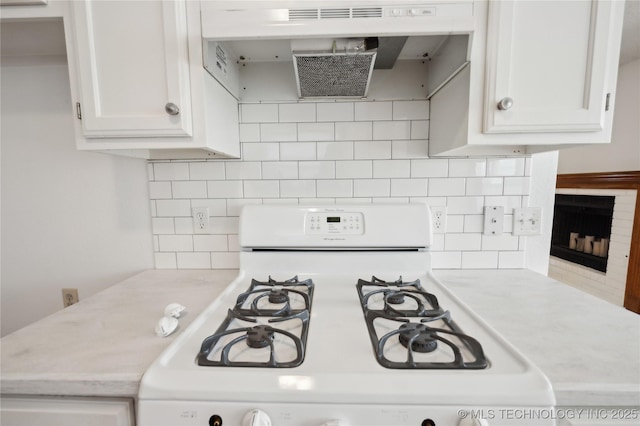 kitchen with decorative backsplash, light countertops, under cabinet range hood, white cabinetry, and white gas range