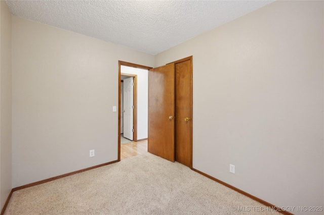 empty room with a textured ceiling, baseboards, and light carpet