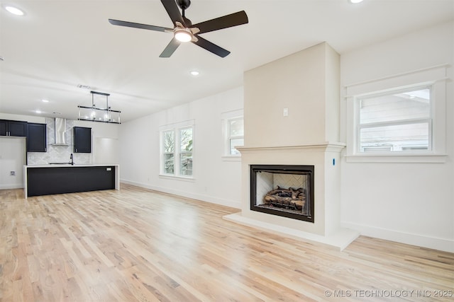 unfurnished living room featuring a fireplace with raised hearth, baseboards, and light wood-style floors