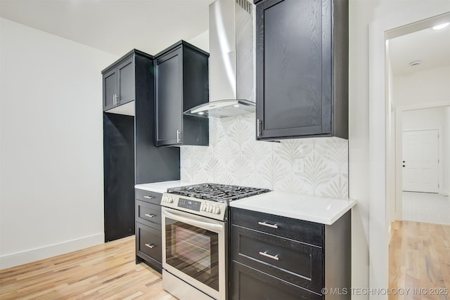 kitchen with gas range, wall chimney range hood, light countertops, and light wood finished floors