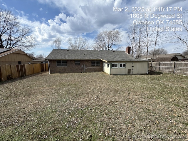 rear view of house featuring brick siding, a fenced backyard, and a chimney