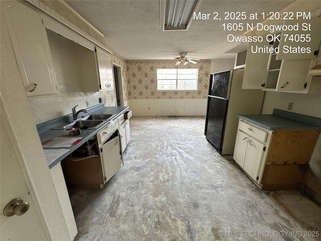 kitchen featuring a wainscoted wall, a sink, a textured ceiling, freestanding refrigerator, and wallpapered walls