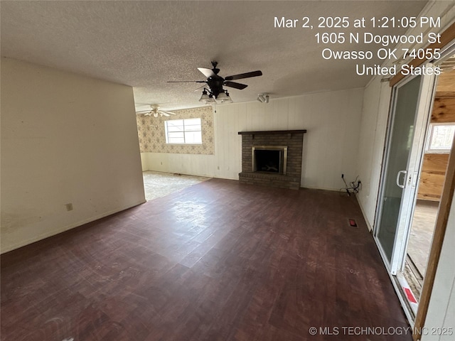 unfurnished living room featuring a ceiling fan, baseboards, wood finished floors, a fireplace, and a textured ceiling