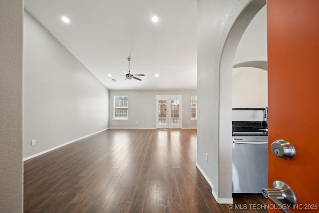 unfurnished living room featuring dark wood-type flooring, baseboards, arched walkways, and ceiling fan