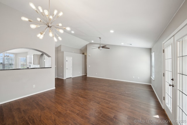 unfurnished living room with lofted ceiling, ceiling fan with notable chandelier, dark wood finished floors, arched walkways, and baseboards