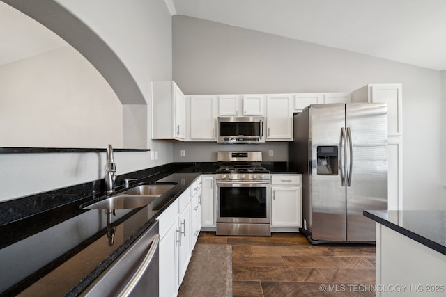 kitchen with vaulted ceiling, white cabinets, appliances with stainless steel finishes, and a sink