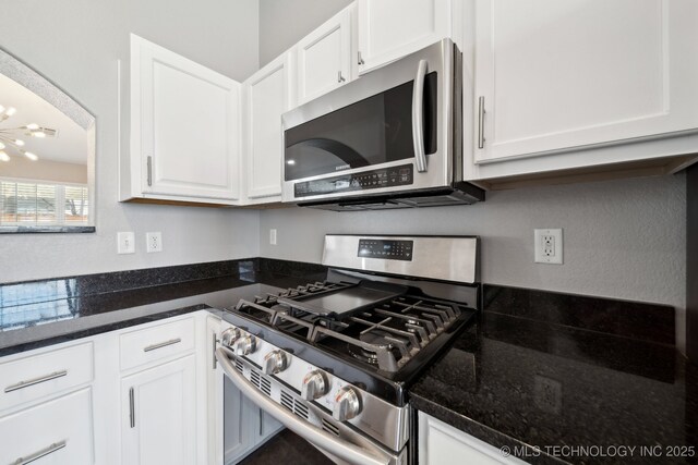 kitchen with a chandelier, dark stone countertops, stainless steel appliances, arched walkways, and white cabinetry