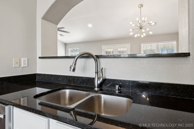 details with dark stone countertops, a sink, white cabinets, decorative light fixtures, and a chandelier