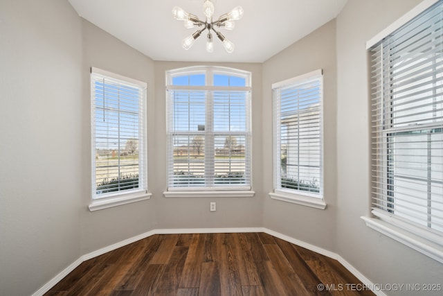 unfurnished dining area featuring a chandelier, dark wood-style floors, and baseboards