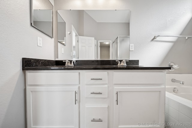 bathroom with tiled bath, double vanity, walk in shower, and a sink