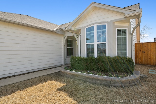 view of side of home with a shingled roof and fence