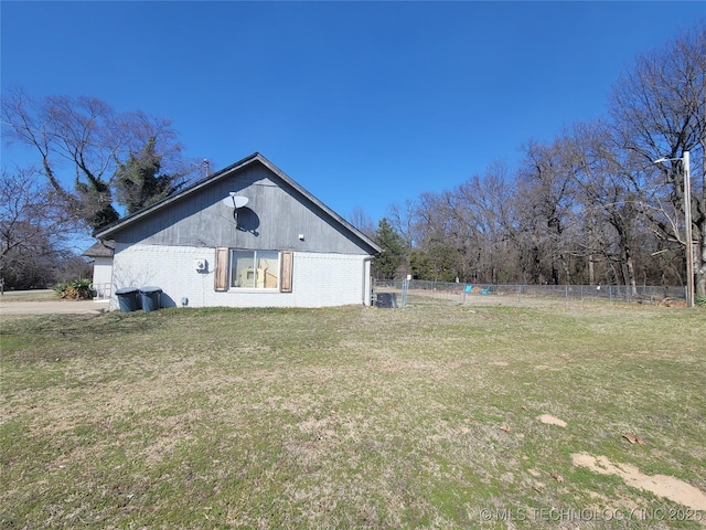 view of property exterior featuring brick siding, a lawn, and fence