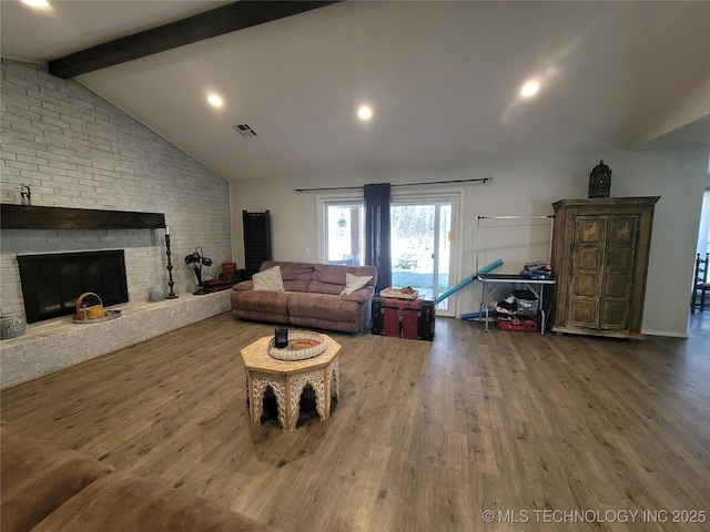 living area with visible vents, a brick fireplace, lofted ceiling with beams, and wood finished floors