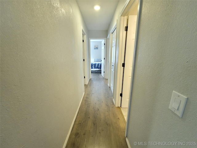 hallway featuring baseboards, wood finished floors, and a textured wall