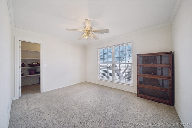 carpeted spare room with baseboards, a ceiling fan, and ornamental molding